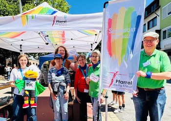 Fünf Personen stehen vor einem Pavillon mit Regenbogenaufdruck.